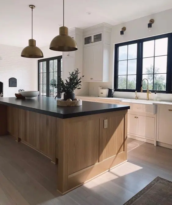 an exquisite modern farmhouse kitchen with white cabinets and a stained kitchen island, black and white countertops, pendant lamps and black frames