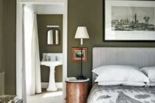 an olive green bedroom with a printed upholstered bed and bedding, a black and white artwork, stained furniture