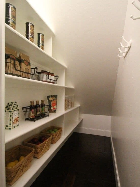 an under stairs pantry with a built-in shelving unit with baskets and wire baskets plus hooks on the walls