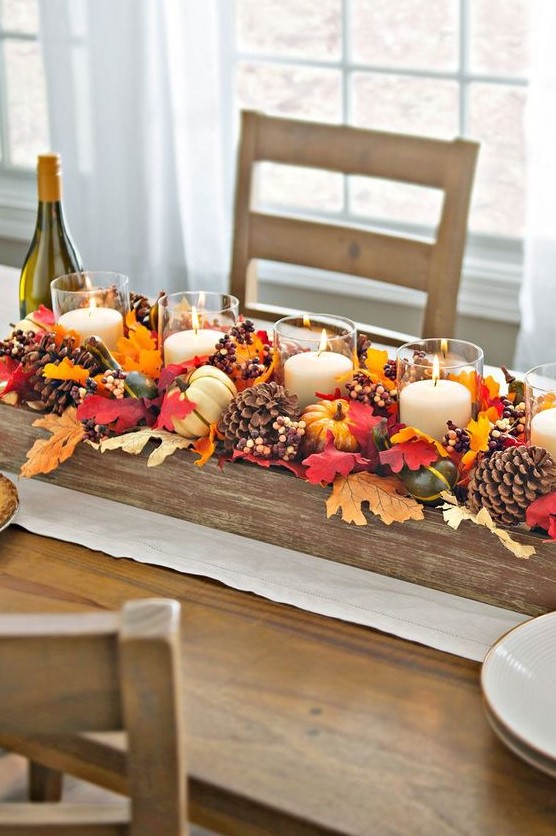 a beautiful Thanksgiving centerpiece of fake fall leaves, pinecones, berries, corn and candles in clear candle holders