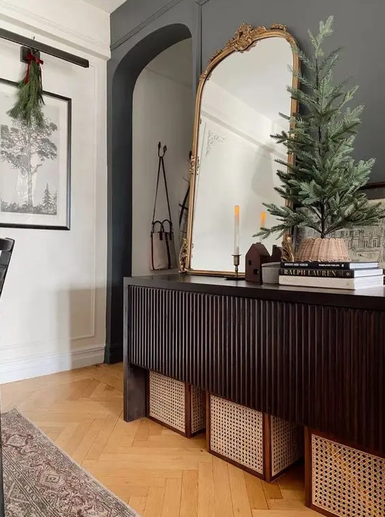 a beautiful dark-stained reeded console table with cane boxes under it, some coffee table books, an arched mirror and a Christmas tree