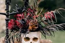 04 a chic vampire Halloween centerpiece of hay, a candleholder, a skull with red roses and thistles, a black candelabra with black candles