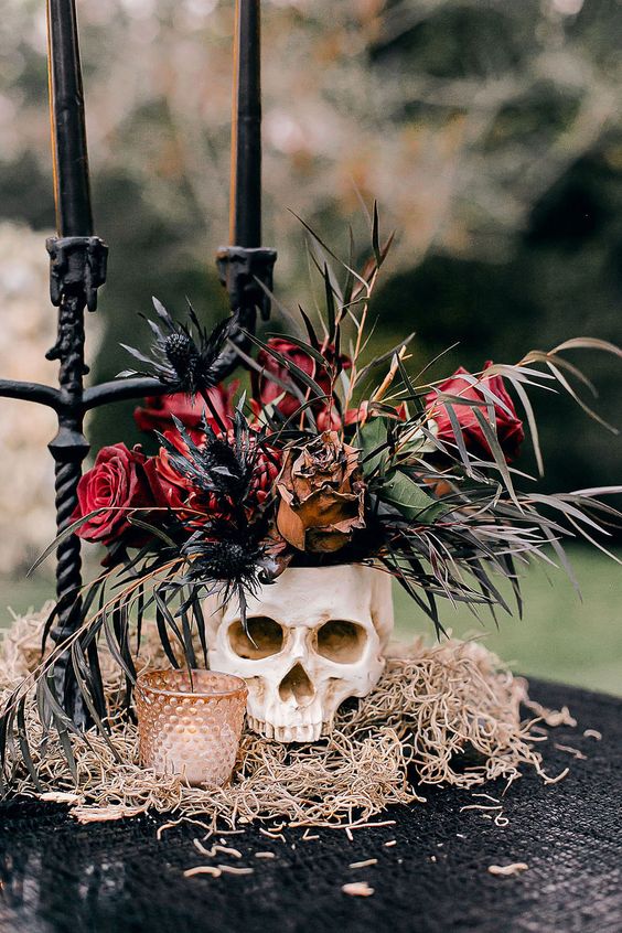 a chic vampire Halloween centerpiece of hay, a candleholder, a skull with red roses and thistles, a black candelabra with black candles