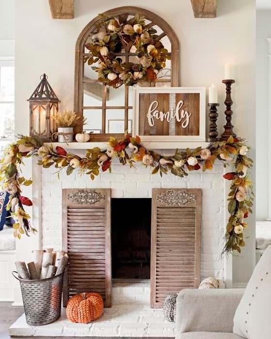 a bright rustic fall mantel with a reclaimed sign, bright leaves and pumpkins, candle lanterns, wooden candleholders with pillar candles and shutters