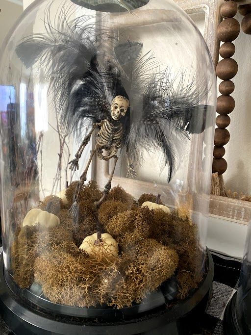 a Halloween cloche with hay, pumpkins and a vampire skeleton figurine is a lovely and catchy idea
