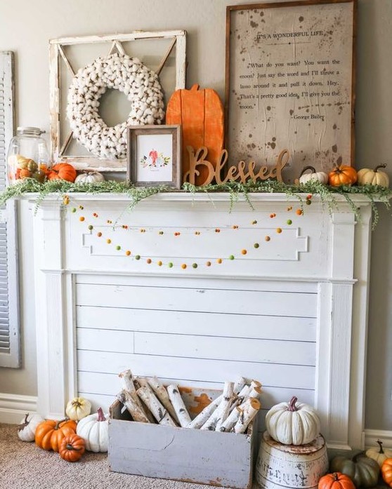 a bright rustic fall mantel with colorful pompom garlands, a crate with birch branches, lots of pumpkins, signs and a cotton wreath