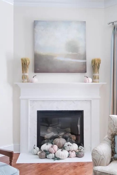 a built in fireplace with pastel and neutral pumpkins in front of it, wheat and pumpkins on the mantel and a lovely artwork