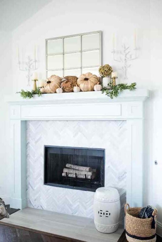 a catchy rustic mantel with faux pumpkins, greenery, dried blooms in a vase, gold candleholders with pillar candles, branch-inspired candleholders on the wall