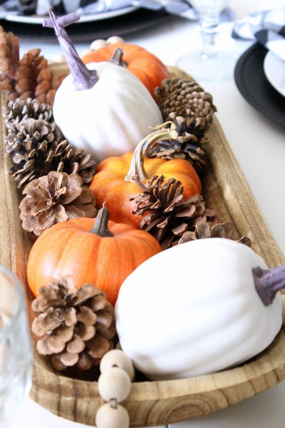 a fall centerpiece of a wooden bowl, pinecones, pumpkins and wooden beads is a cool idea for fall decor