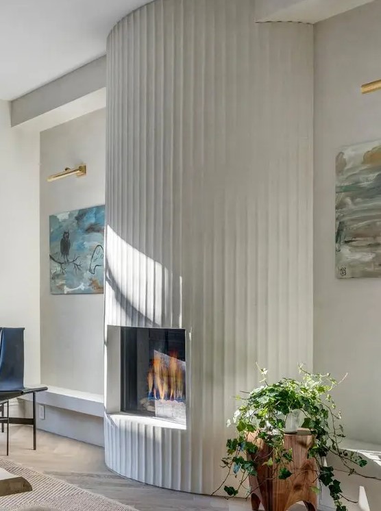 a fireplace with a curved fluted surround, a potted plant, beautiful artwork and a black chair are a cool combo for a modern living room
