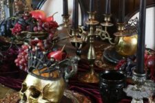08 a jaw-dropping vampire Halloween tablescape in burgundy, black and gold, with a skull in a crown, some fruit and black candles