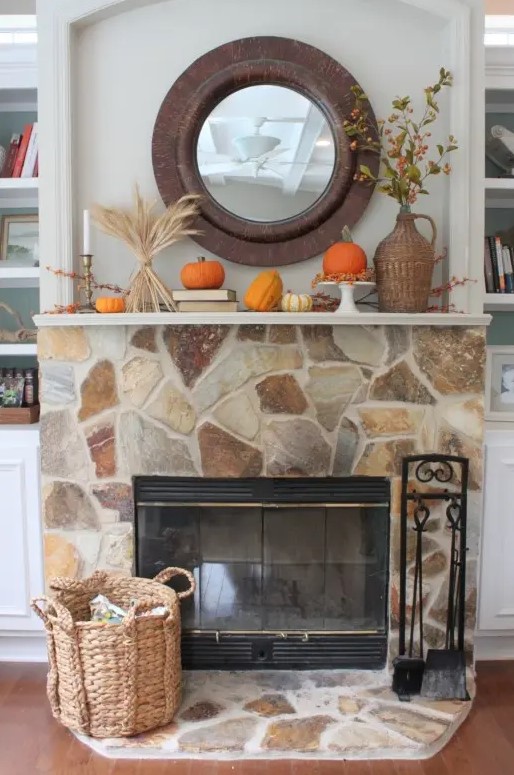 a chic fall mantel styled with wheat, berries, pumpkins and gourds, berry branches in a wicker vase plus a basket next to the fireplace