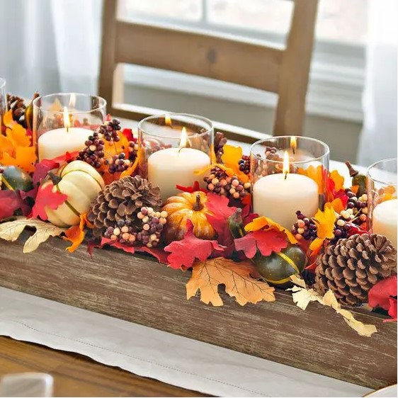 a fall centerpiece of a wooden box with pinecones, faux leaves, berries, faux gourds and candles is a bold idea