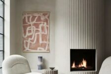 10 a fireplace with a fluted surround, neutral curved chairs, a bold printed rug and a bold artwork look so chic together