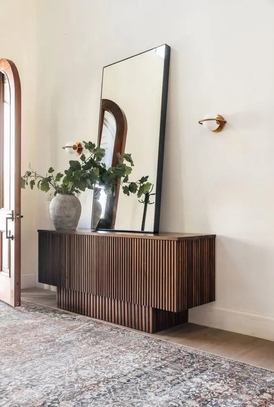 a cool stacked reeded console table with an oversized mirror, a planter with greenery and a sconce is a cool idea