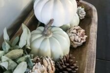 11 a fall decoration of a wooden bowl with pinecones, white faux pumpkins, green balls and pale leaves