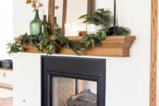 13 a cool rustic fall mantel with a greenery garland, green bottles with dried blooms, empty frames, mirrors, firewood and stacked heirloom pumpkins
