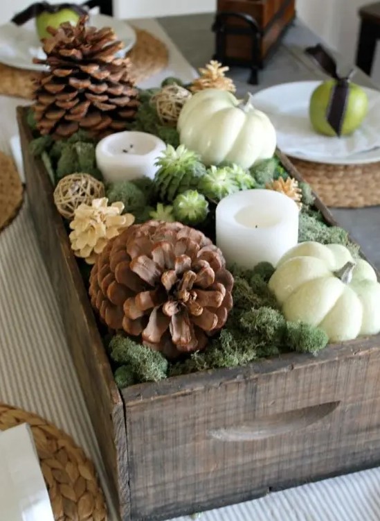 a gorgeous fall centerpiece of a crate with moss, succulents, candles, usual and bleached pinecones and pumpkins