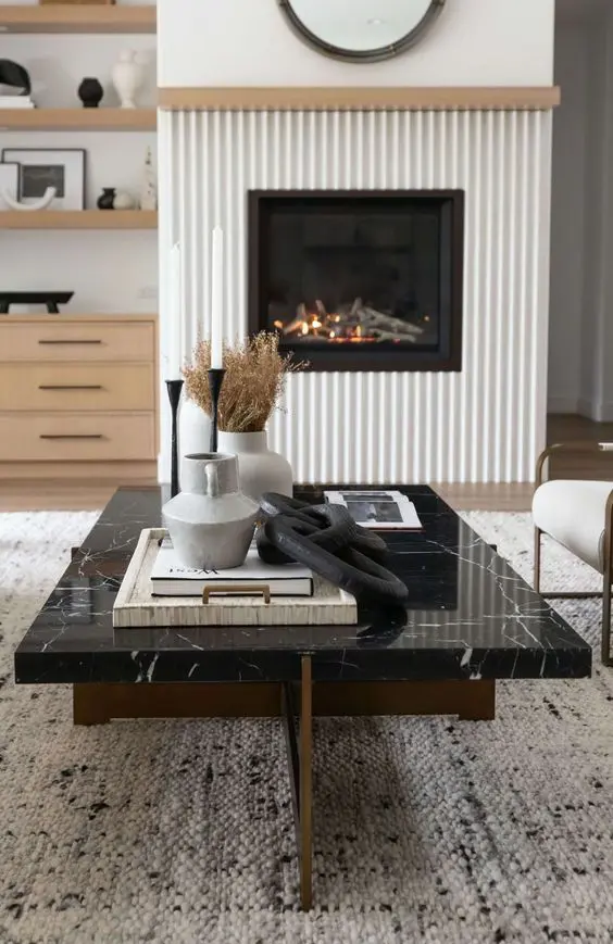 a modern fireplace with a fluted surround, a black marble coffee table with decor and neutral furniture