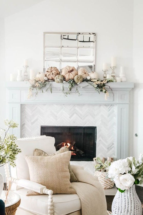 a delicate neutral fall rustic mantel with faux pumpkins, greenery, neutral faux blooms, pillar candles in silver candleholders is chic