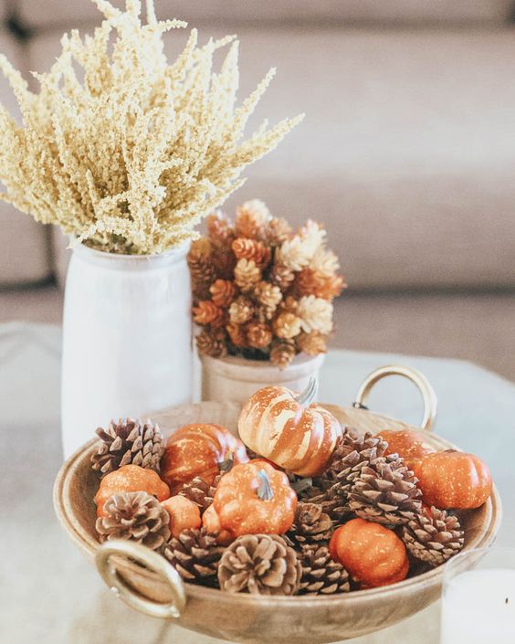 a lovely fall centerpiece of a bowl with faux pumpkins and pinecones, grasses in a jar and a planter with pinecones