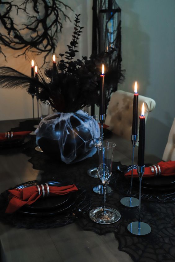 a sophisticated vampire Halloween tablescape in red and black, with a black lace runner, burgundy candles and skeleton hand glasses