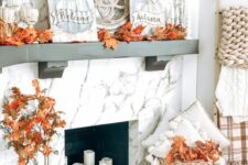 17 a fall mantel with candles, bright faxu leaves, pumpkins, a basket with pillows and branches and branches in a bottle