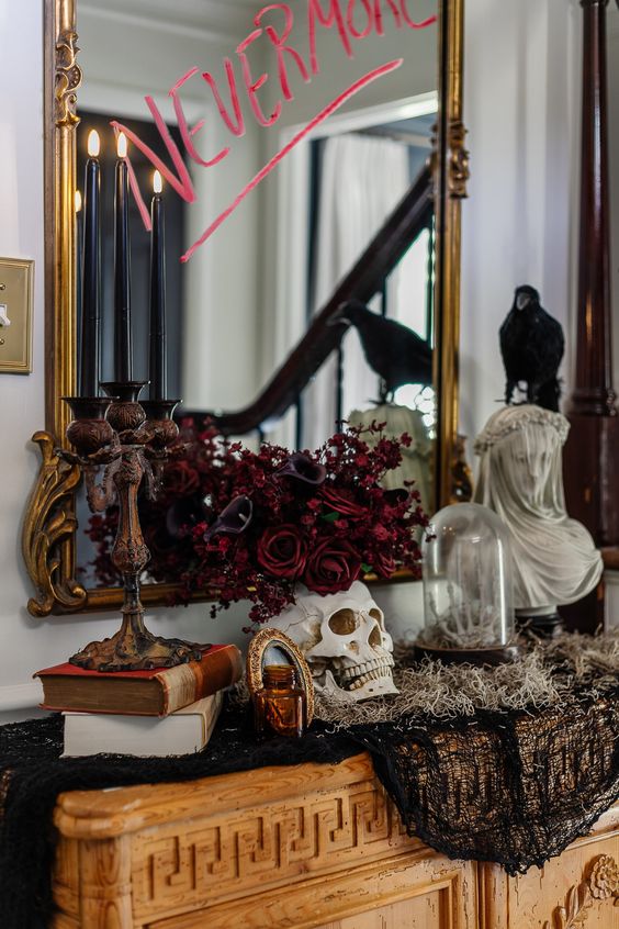 a refined Halloween console table with books, a candelabra, a skull with red and deep purple blooms and black cheesecloth