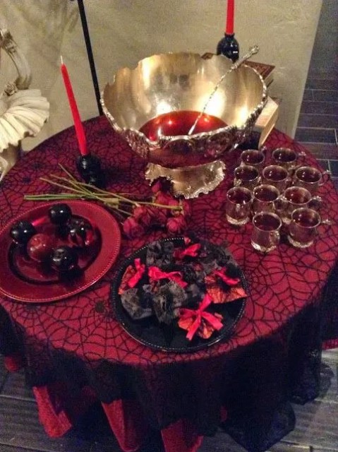 an elegant punch table with bloody punch and bloody apples, black and red candles