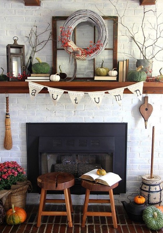 a lovely rustic fall mantel with bold pumpkins, a wreath with berries, a candle lantern, branches in planters and books is all cool