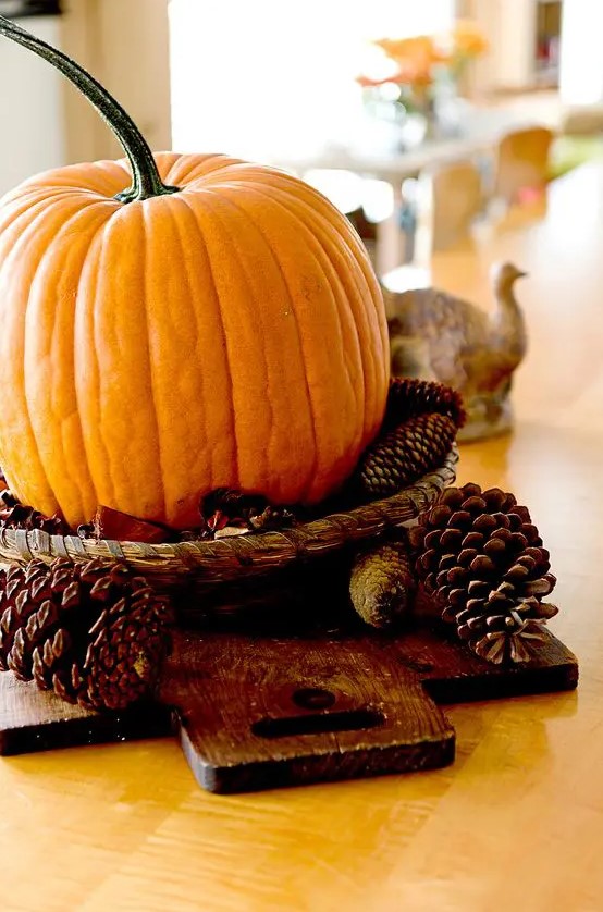 a simple fall centerpiece of a wood board, pinecones and a pumpkin in a woven tray is easy to make