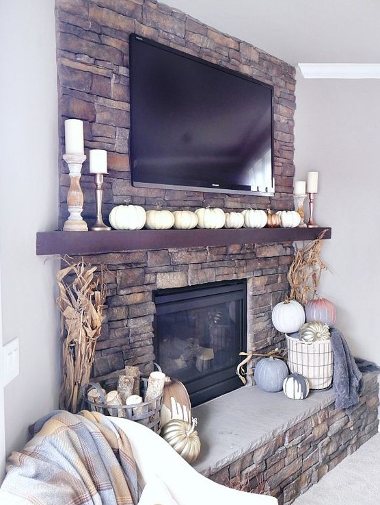 a lovely rustic fall mantel with lots of faux pumpkins, corn husks, pillar candles, a basket with pumpkins and blankets