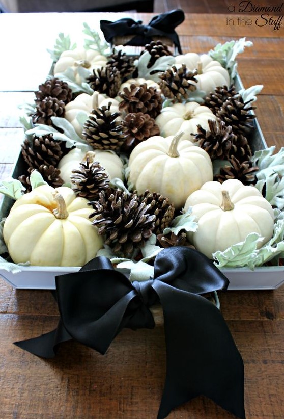 an elegant fall centerpiece of pale greenery, white pumpkins, pinecones and black silk bows