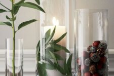 29 tall glasses with acorns and pinecones and a pillar candle and greenery for decorating for the fall in a modern way