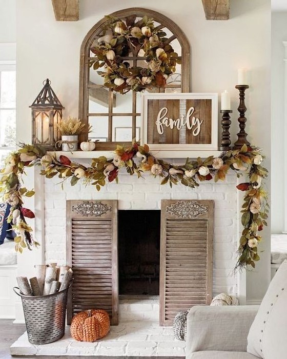 a rustic fall mantel with dried fall leaves and pumpkins, candles in wooden candle holders, wheat arrangements and a rustic sign