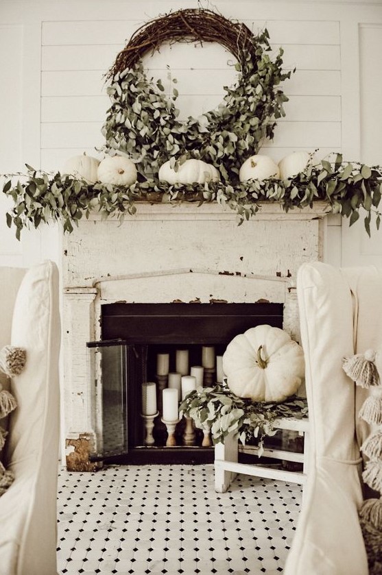 a shabby chic and rustic fall mantel with greenery, white pumpkins, a lush wreath with greenery and candles in the fireplace