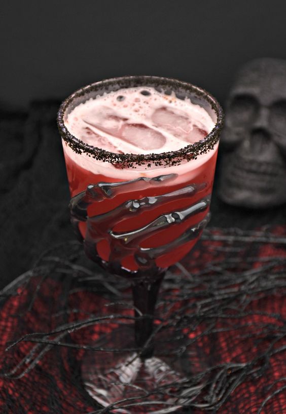 a red Halloween cocktail in a spectacular skeleton hand glass with black rim is a stunning idea for a vampire party