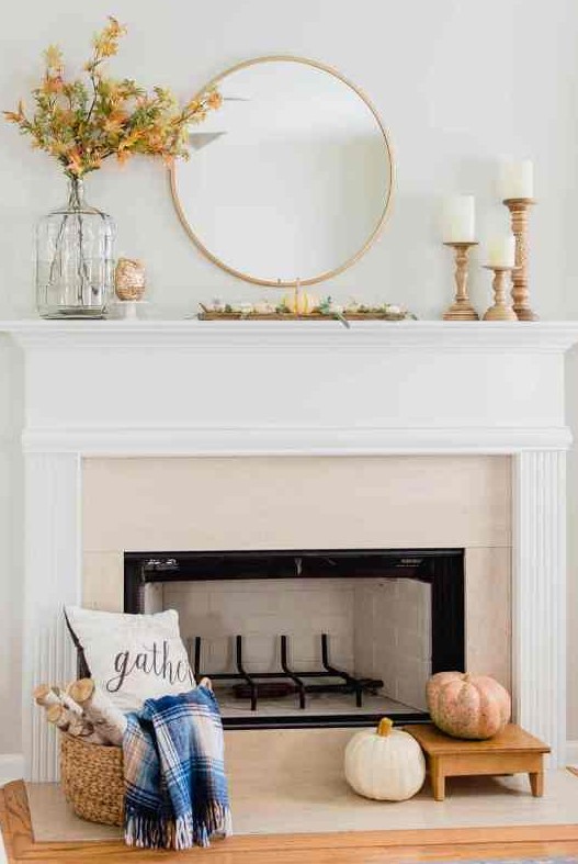 a simple and lovely rustic mantel with faux pumpkins and greenery, bold dried leaves, pillar candles in wooden candleholders