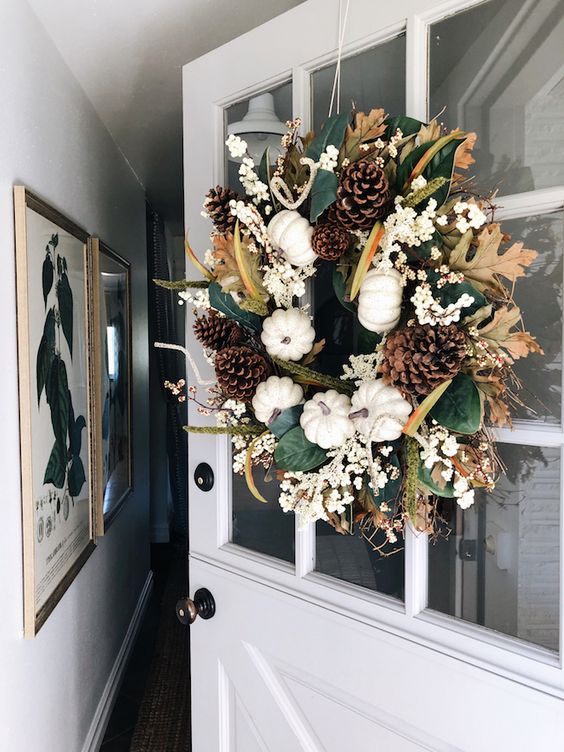 a fall wreath of pumpkins, leaves, white blooms, pinecones and twigs is a lovely rustic decoration