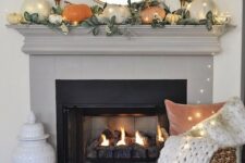 35 a simple contemporary fall mantel done with greenery and pumpkins of muted colors plus lights all over it