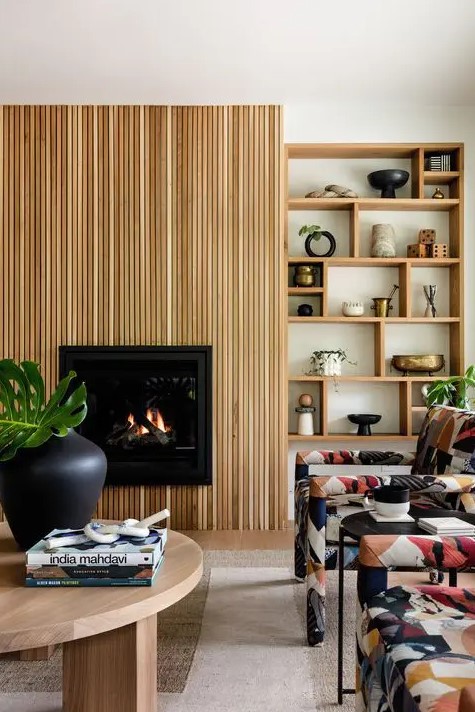 a modern living room with a shelving unit, a fireplace with a reeded surround, a low coffee table and colorful chairs