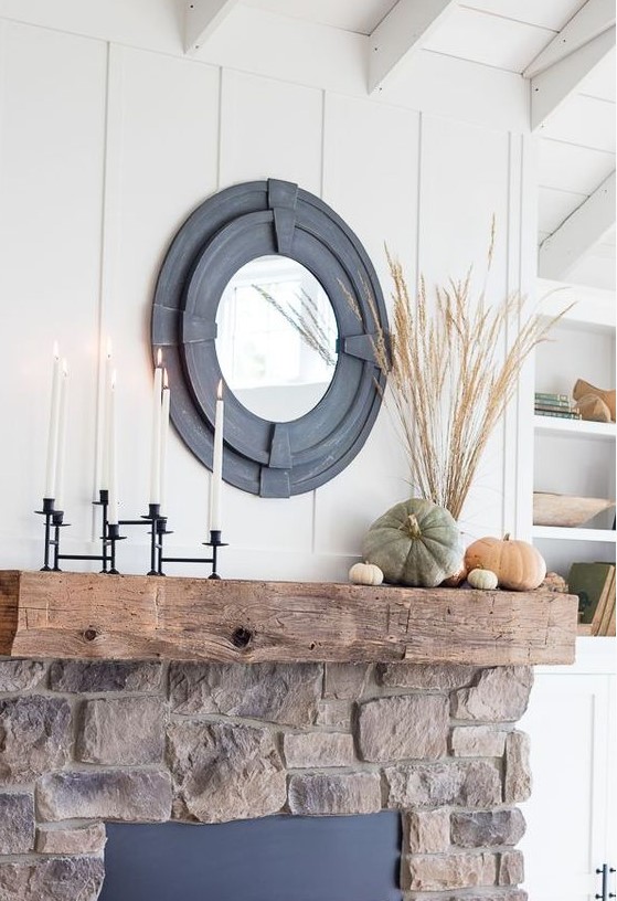 a stylish rustic fall mantel with a black candelabra with tall candles, natural heirloom pumpkins and wheat in a vase plus a mirror in a cool black frame