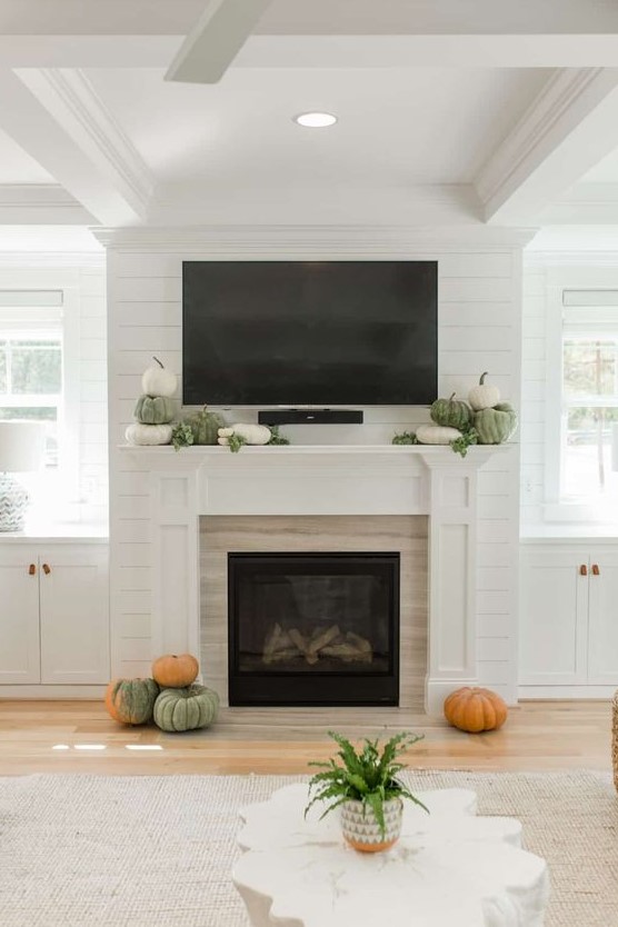a very simple and laconic fall mantel with heirloom pumpkins stacked and some greenery plus some pumpkins around the fireplace
