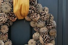 38 a simple and cool fall to winter wreath of pinecones, with a gold ribbon, is a stylish decoration to make