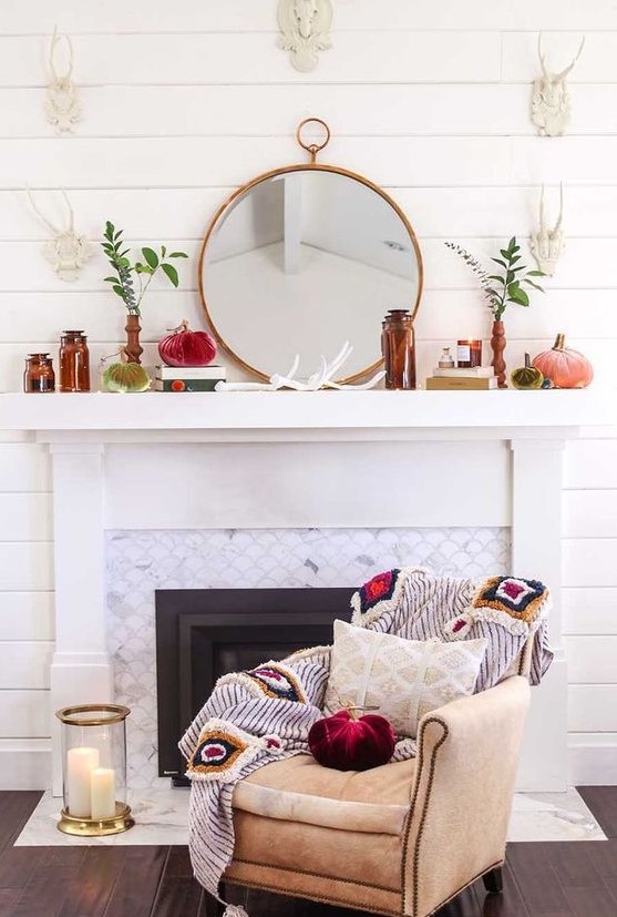 a whimsy fall mantel with brown bottles, a round mirror, greenery in vases, velvet pumpkins
