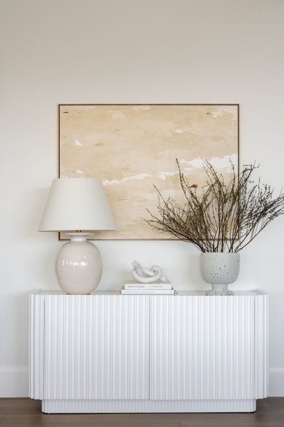an elegant white fluted piece with a table lamp, a vase with branches and coffee books is a cool idea for any entryway
