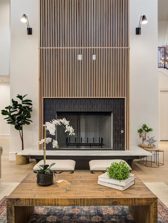 a modern living room with a fireplace with a brick and fluted surround, a wooden coffee table and potted greenery