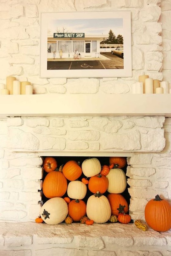 a white faux stone fireplace filled with white and orange pumpkins and gourds plus pillar candles on the mantel is a lovely idea