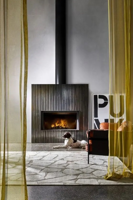 a modern space with a fireplace and a fluted surround, an orange leather chair, a printed rug and some cool decor