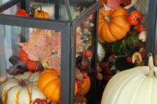42 a black lantern filled with pinecones and fake pumpkins, berries and leaves for a bright fall display